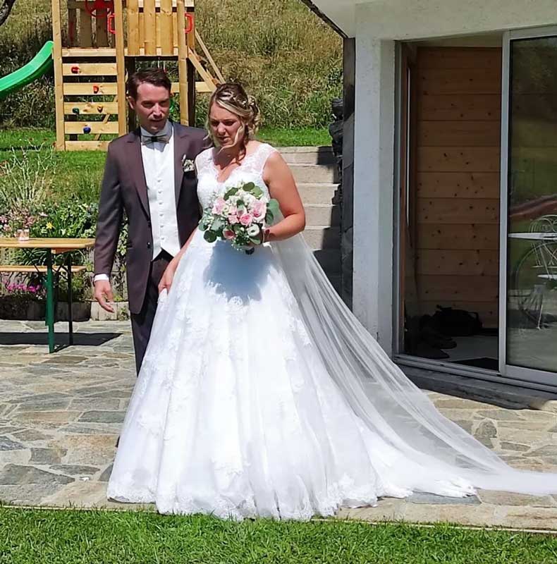 femme portant un bouquet de fleur en robe de mariée cymbeline annecy au bras de son mari